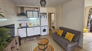 Un espacio habitable compacto con kitchenette, un sofá con cojines amarillos y una pequeña mesa redonda.