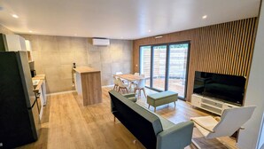 A modern living space with a kitchen, dining area, and a large TV screen. - New 3-bedroom villa + SPA (Labenne)