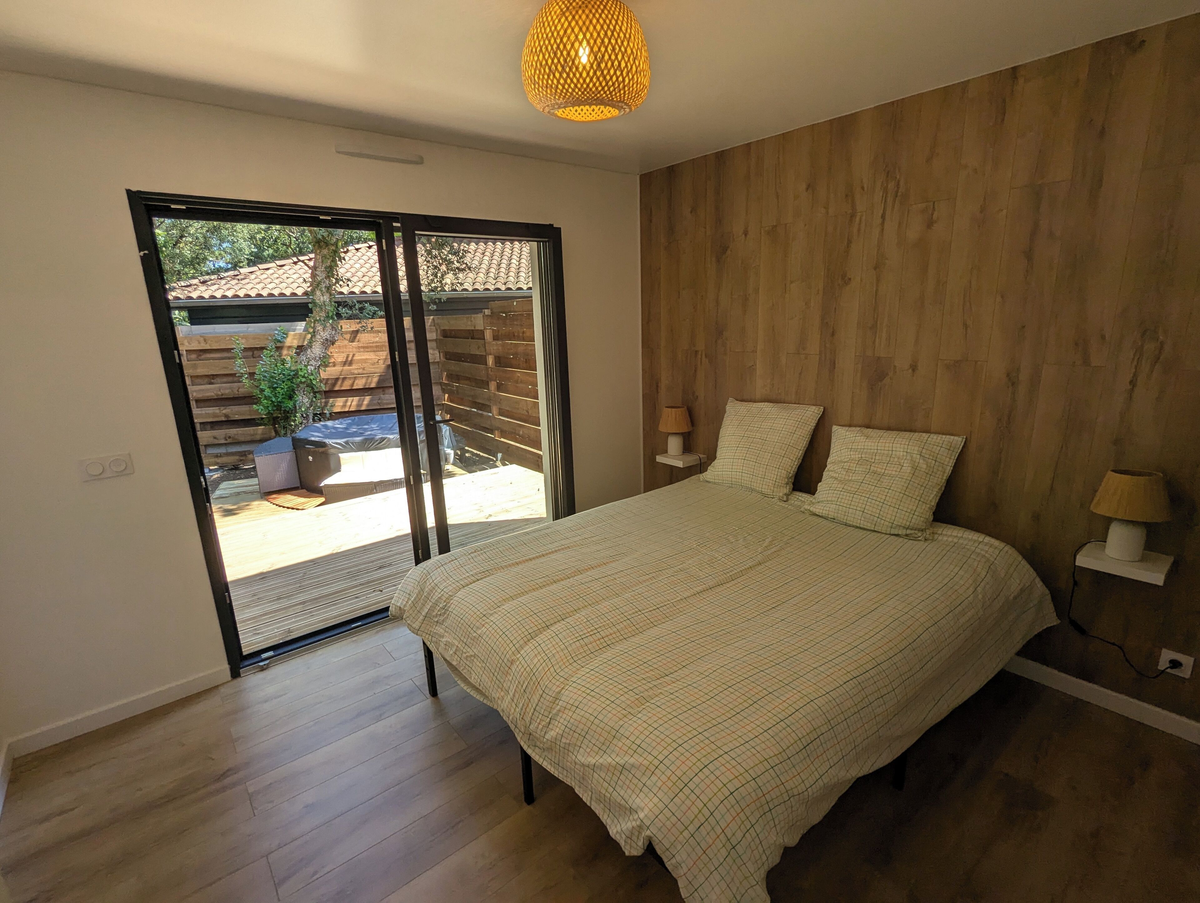 A bedroom with a large bed, wooden walls, a sliding glass door to a patio, and a hanging light fixture.