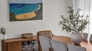 Ein Essbereich mit Holztisch, Stühlen, einem großen Gemälde von einem Strand und einer Topfpflanze.