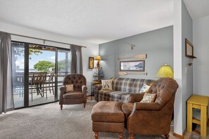 A living room with a brown leather sofa, a brown armchair, a plaid sofa, and a dining area with a table and chairs.