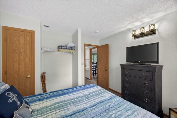 Une chambre à coucher comprenant un lit, une commode, un téléviseur et un couloir menant à une autre pièce.
