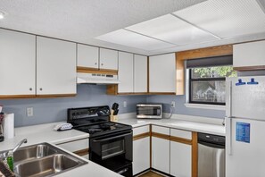 A compact kitchen with a stove, microwave, and refrigerator, featuring white cabinets and a window.