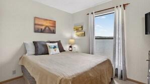 Une chambre à coucher avec un lit, une table de chevet, une lampe, un tableau et une vue sur l’eau.