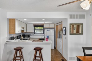 A modern kitchen with white cabinets, a microwave, and a refrigerator. There are two wooden stools at the island.