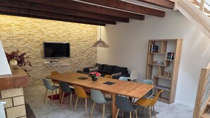 Un espace repas comprenant une table en bois, des chaises, un canapé, un téléviseur et une bibliothèque.