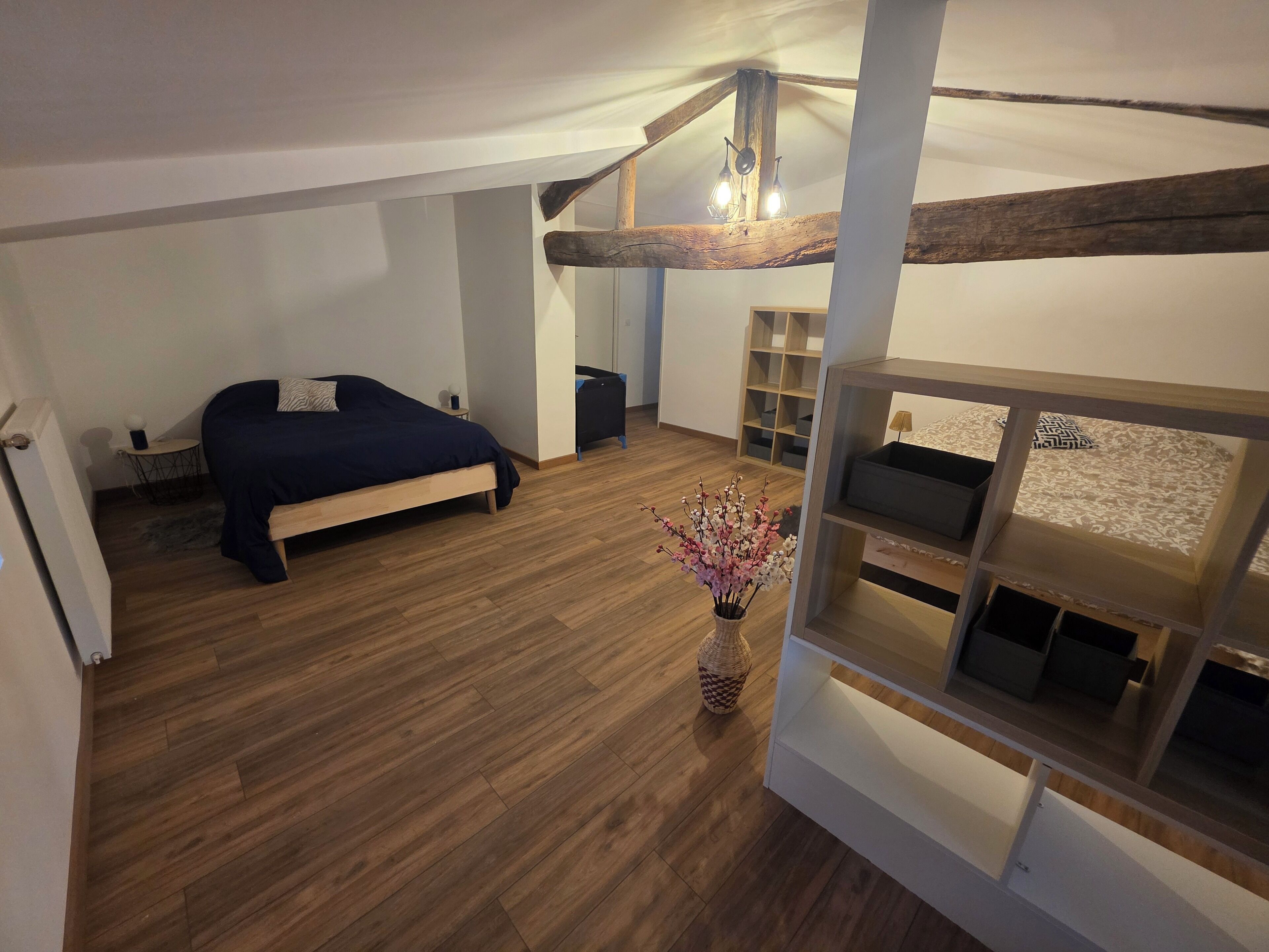 A bedroom with a bed, bedside tables, a wooden floor, a ceiling with exposed beams, and a hanging light fixture.