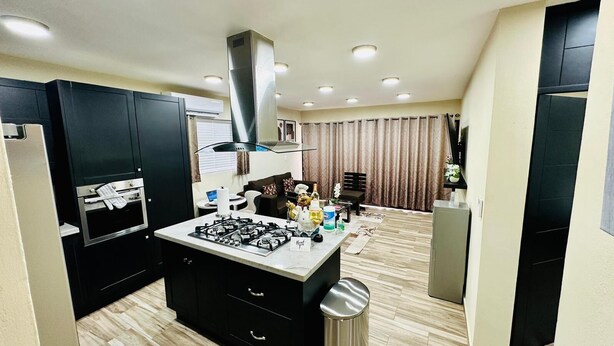 Cocina compacta con una isla central, horno empotrado y extractor de acero inoxidable.