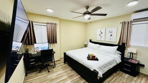 Habitación de hotel con cama, escritorio con computadora, ventilador de techo y ventana con cortinas.