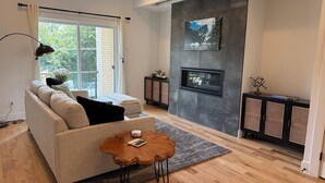 A modern living room with a sofa, a coffee table, a fireplace, and a large window.