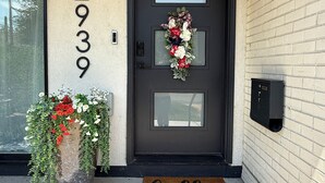 A front door with a black number plate, a welcome mat, and a potted plant with flowers.