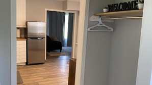 Een gang die leidt naar een keuken met een koelkast, een eethoek met een tafel en stoelen, en een kast met een 'WELCOME' bord.