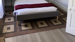 Een keurig opgemaakt slaapkamer met een groot bed, twee nachtkastjes, een raam en een deur.