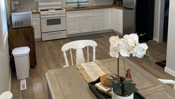 Een moderne keuken met witte kasten, een zwarte koelkast en een eethoek met een tafel voor twee personen.
