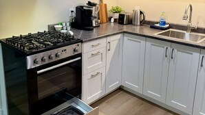 Une cuisine moderne avec des meubles blancs, une hotte en acier inoxydable, une cuisinière à gaz, un four et un évier.