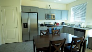 A kitchen with grey cabinets, a stainless steel refrigerator, a microwave, a stove, and a dishwasher. There is a wooden dining table with four chairs. - Charming 3-bedroom house in nice Merced (Merced)