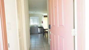 A hallway with a pink door, a tiled floor, and a rug leading to a kitchen area. - Charming 3-bedroom house in nice Merced (Merced)