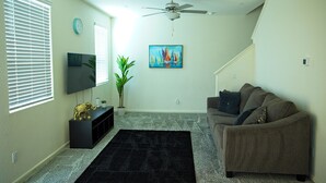 A living room with a flat-screen TV, a ceiling fan, a black rug, a brown couch, and a painting on the wall. - Charming 3-bedroom house in nice Merced (Merced)