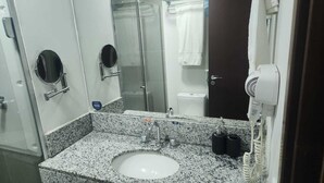 A bathroom with a granite countertop sink, a mirror, a towel rack, a hand dryer, and a glass shower enclosure. - Rio Centro/Barra Olímpica Suite (Jacarepaguá Rio de Janeiro)
