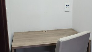 A corner desk with a light brown finish, a white cushioned chair, and a 110V electrical outlet on the wall. - Rio Centro/Barra Olímpica Suite (Jacarepaguá Rio de Janeiro)