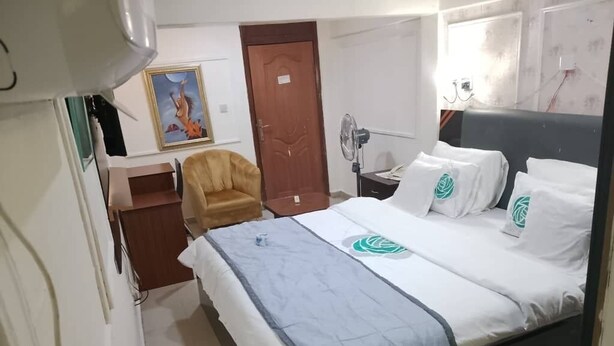 A hotel room with a bed, a chair, a desk, and a wall-mounted TV. - Kenbrill Hyatt Hotel (Benin City)