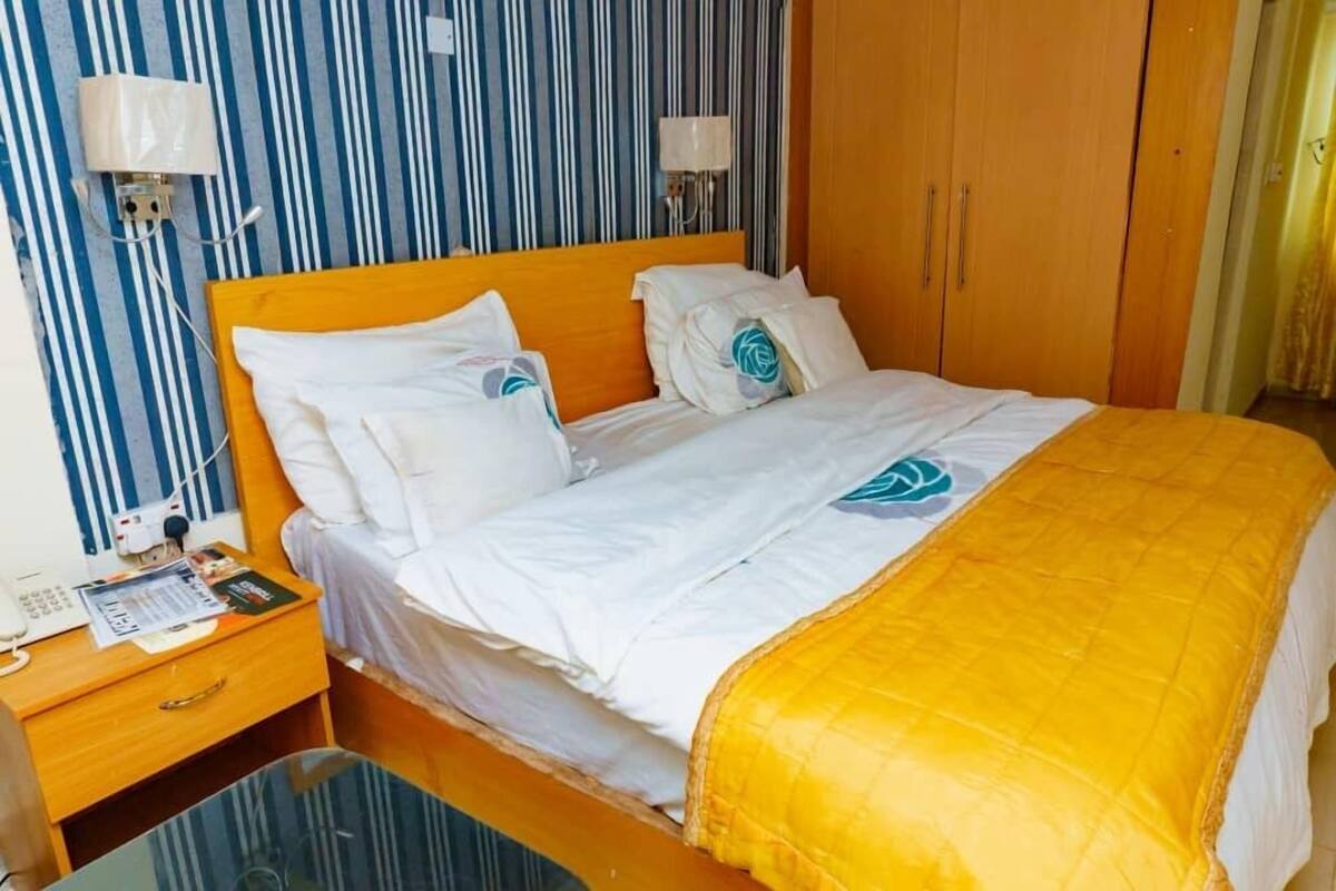 A hotel room with a bed, a nightstand with a telephone and papers, and a wardrobe.