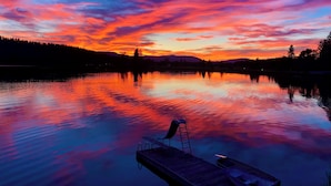 Um lago calmo ao pôr do sol, com um píer de madeira e um pequeno barco.