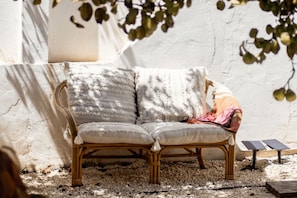 A wicker sofa with cushions against a textured wall, a small table, and a plant.