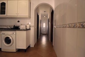A laundry area with a washing machine, cabinets, and a tiled hallway leading to a door.