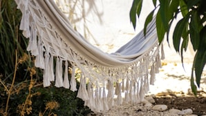 Una hamaca con flecos de macramé, frente a un entorno natural con plantas y rocas.
