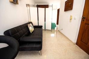A modern living room with a black sofa, a standing lamp, and a wooden door.