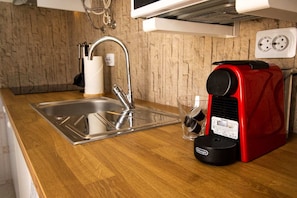 A kitchen with a stainless steel sink, a red coffee maker, and a clear glass.