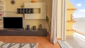 En moderne stue med et fladskærms-tv, et minimalistisk konsolbord og et stort vindue med gardiner.