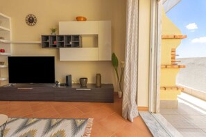 A modern living room with a flat-screen TV, a minimalist console table, and a large window with curtains.