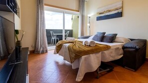 A hotel room with a bed, a sofa, a TV, a table, and a view of the outdoors.
