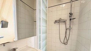 Une salle de bain avec un lavabo blanc, un miroir et une douche équipée d’un pommeau de douche à main.