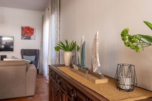 A living room with a sofa, a TV, a plant, and decorative items on a wooden dresser.