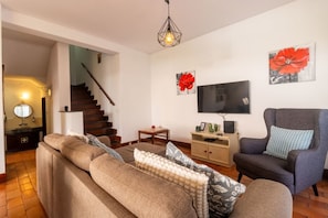 A living room with a sofa, armchair, TV, and artwork on the wall.