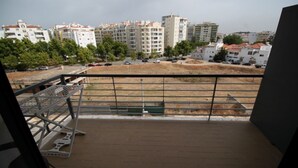 En balkon med gelænder i metal, murstensgulv og udsigt til omkringliggende bygninger samt en parkeringsplads.