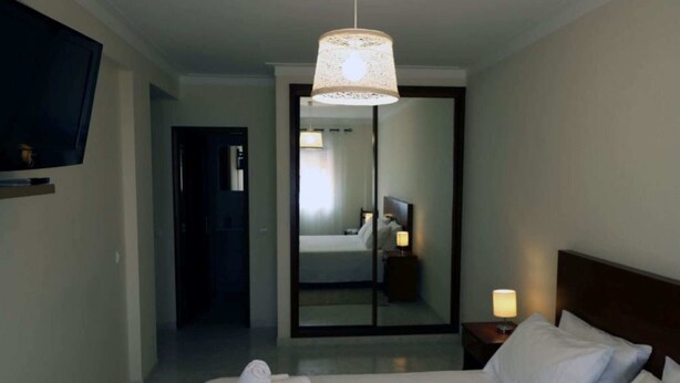 Et hotelværelse med en seng, et fjernsyn, et spejl og et natbord med en lampe.