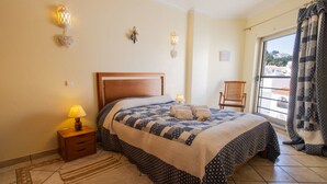 Ein Schlafzimmer mit Bett, Nachttisch, Lampe und Blick ins Freie.