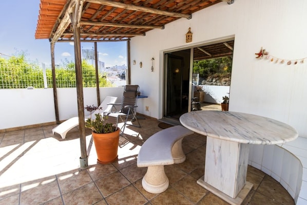 A covered patio with a table and chairs, a potted plant, and a view of the city.