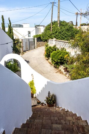 A residential area with a paved driveway, a stone wall, and a white building with a curved facade. - Casa do Mar by Urban Beach Rentals (Vale Centianes - Carvoeiro -Lagoa)