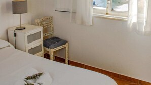 Un dormitorio con cama, una silla, mesita de noche, lámpara y ventana con vista al mar.