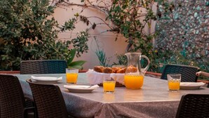 Una mesa para comer al aire libre con platos, vasos y una jarra de jugo de naranja, rodeada de sillas de mimbre.