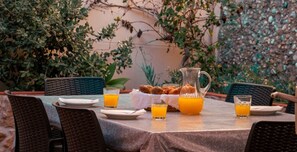 An outdoor dining table with plates, glasses, and a pitcher of orange juice, surrounded by wicker chairs.