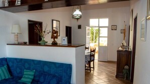 Una sala de estar con un sofá azul, un mostrador de recepción de madera, una zona de comedor con una mesa y sillas, y un ventanal grande.