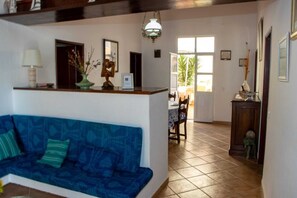 A living room with a blue sofa, a wooden reception desk, a dining area with a table and chairs, and a large window.