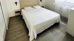 A bedroom with a bed, bedside tables, a hanging light fixture, and a window with blinds.