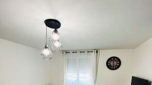 A modern living room with a sofa, a coffee table, a small ottoman, a black TV stand, and a ceiling light fixture.